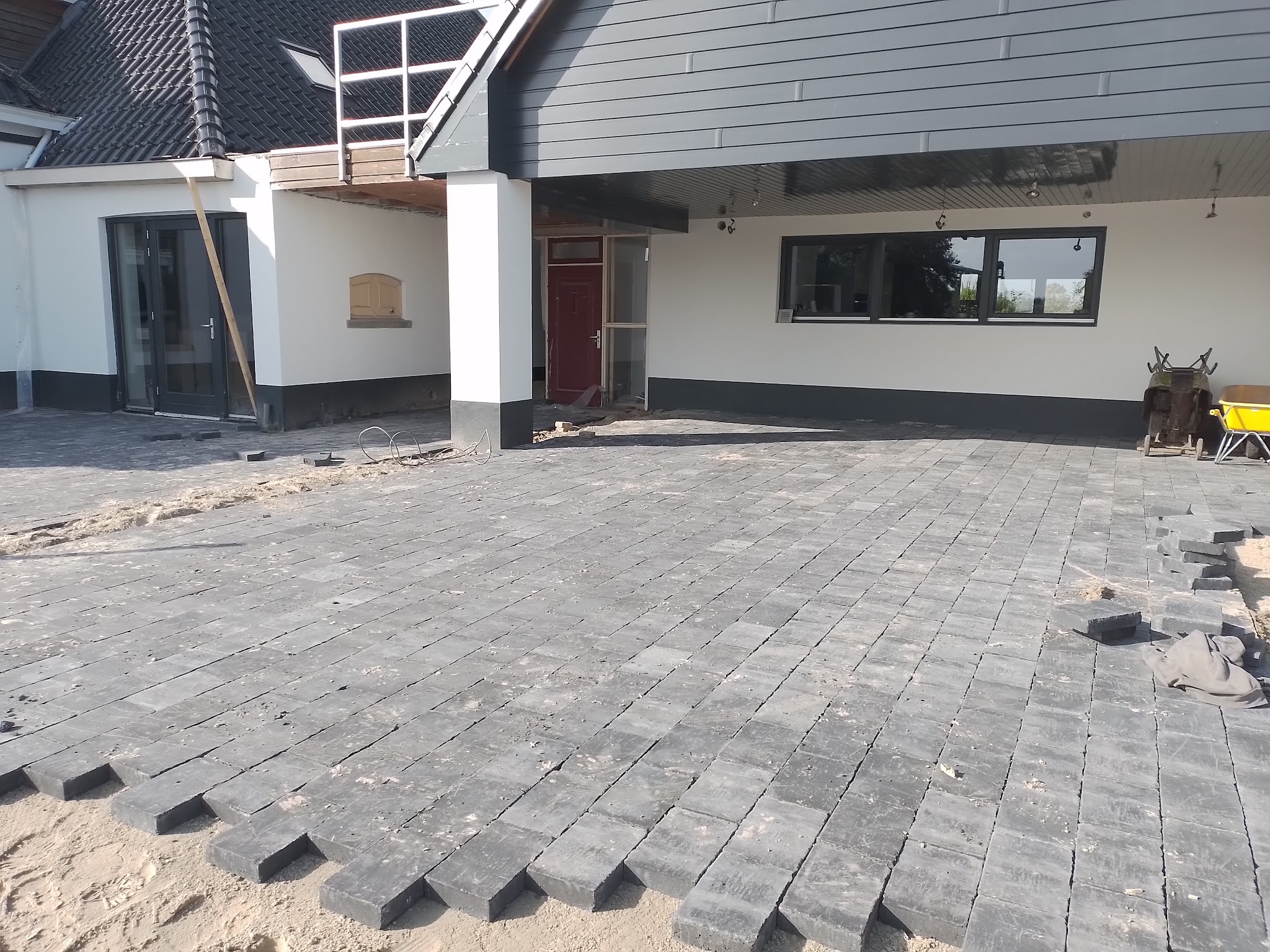 Antraciet bestrating onder een overdekte entree van een wit gestucte boerderij